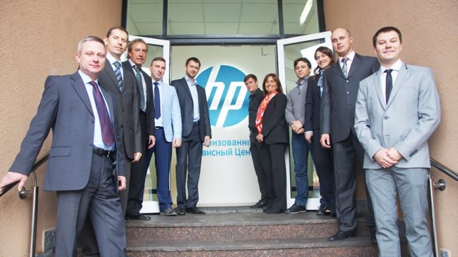 Thirteen people on the porch of a service center by a glass door carrying an HP Authorised Service Center logo